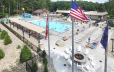 aerial view of Cascade Cove Aquatic Park and bonfire area on pool deck, American and Canada flags blowing in wind in forground