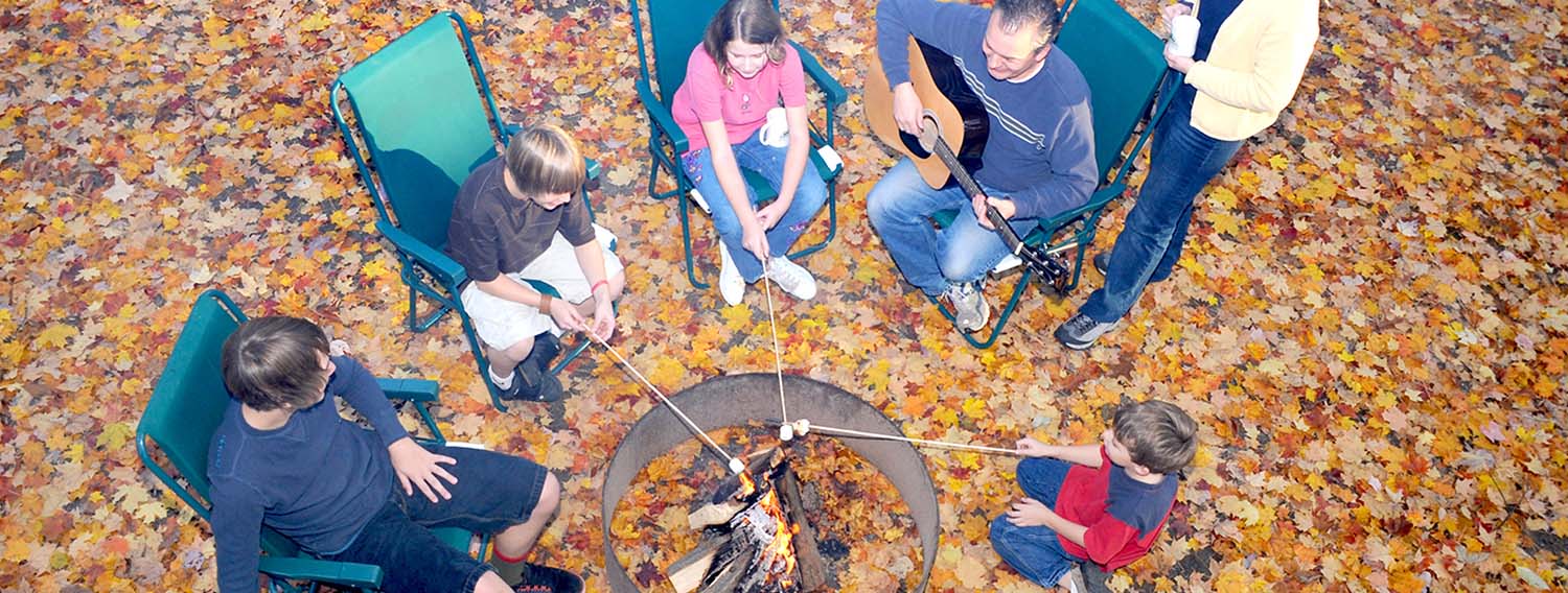 Guests roasting marshmallows over campfire surrounded by fall colored leaves