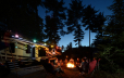 family sitting by campfire in front of RV at sunset under trees