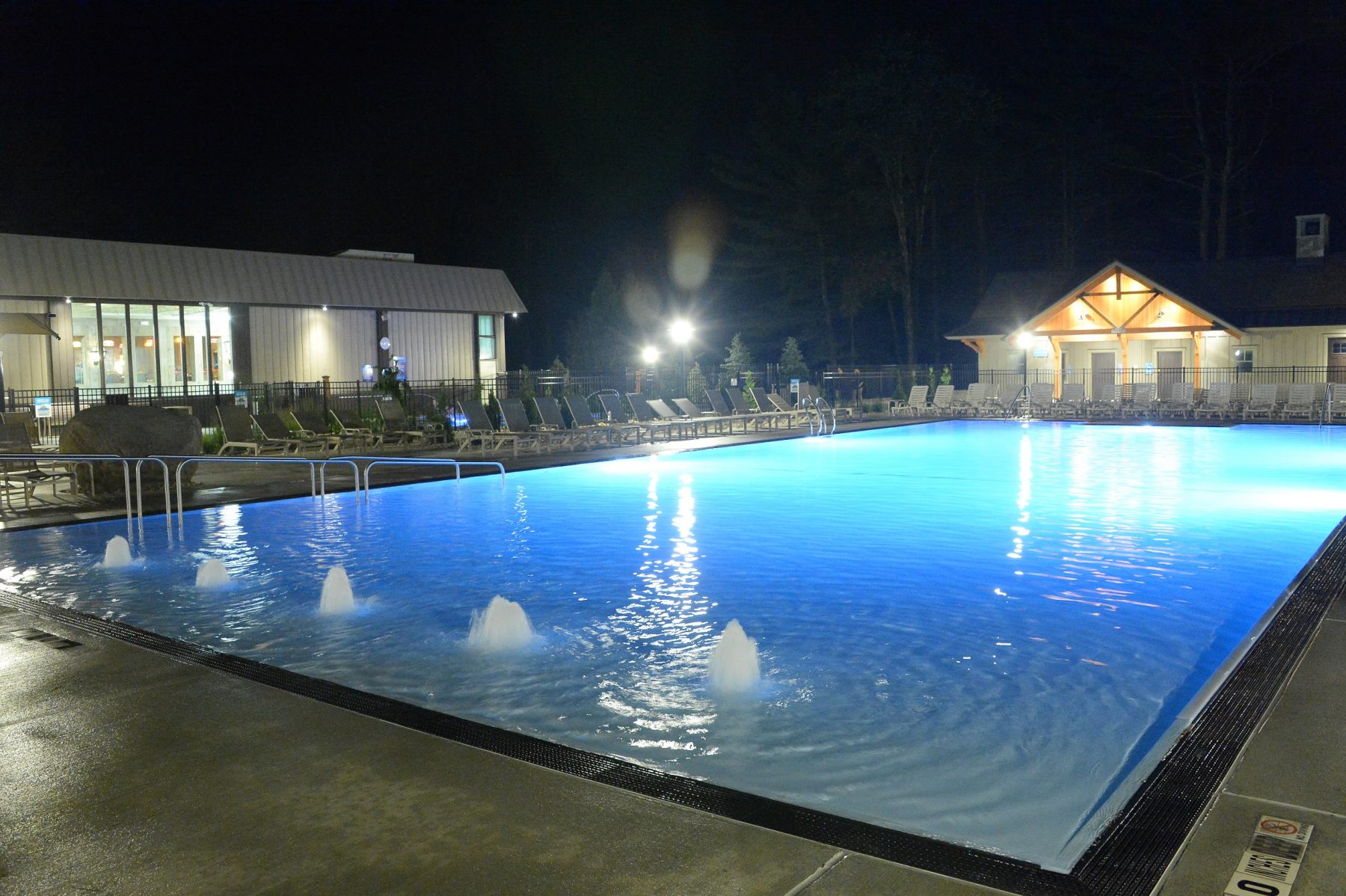 The zero entry pool is shown at night in the foreground. The east building and bathrooms are shown in the background.