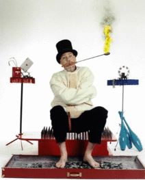 French Mountain Playhouse artist Doc Swan, sitting on a bed of nails in a straight jacket with a top hat on and a flaming stick coming out of his mouth