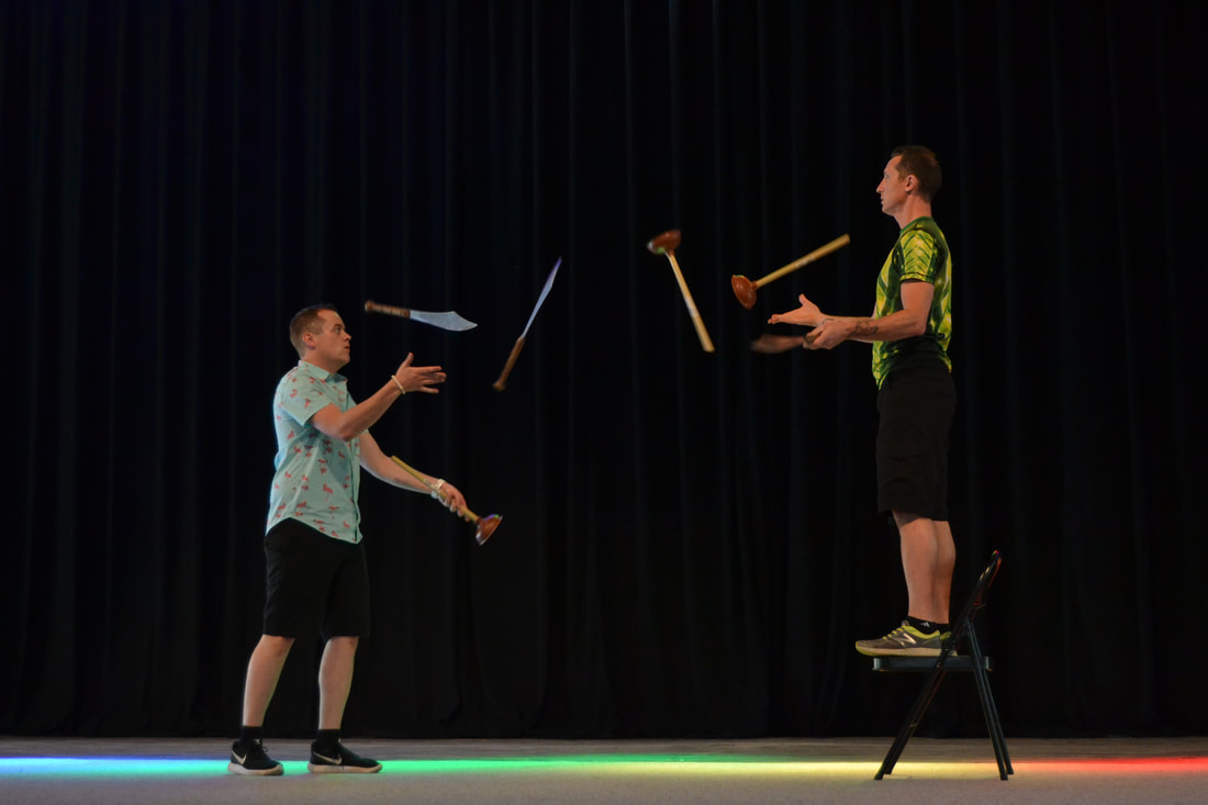 Two men are juggling plungers and knives