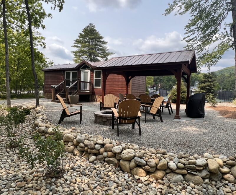 Outdoor set up of cabins including a patio, pavilion, a firepit and plenty of chairs as well as a Weber Grill