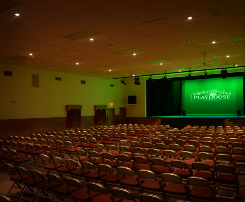 Inside of our French Mountain Playhouse with green lighting effects and "French Mountain Playhouse" logo displayed at center stage.