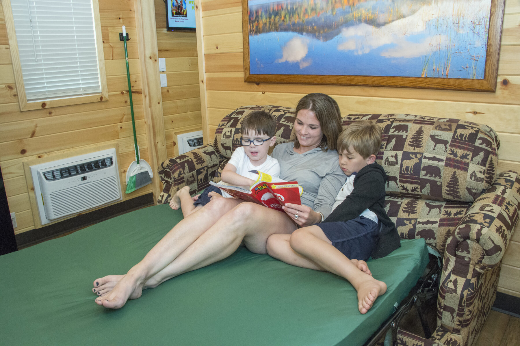 Mother reading a book to her two sons on the sleeper sofa in one of our new cabins